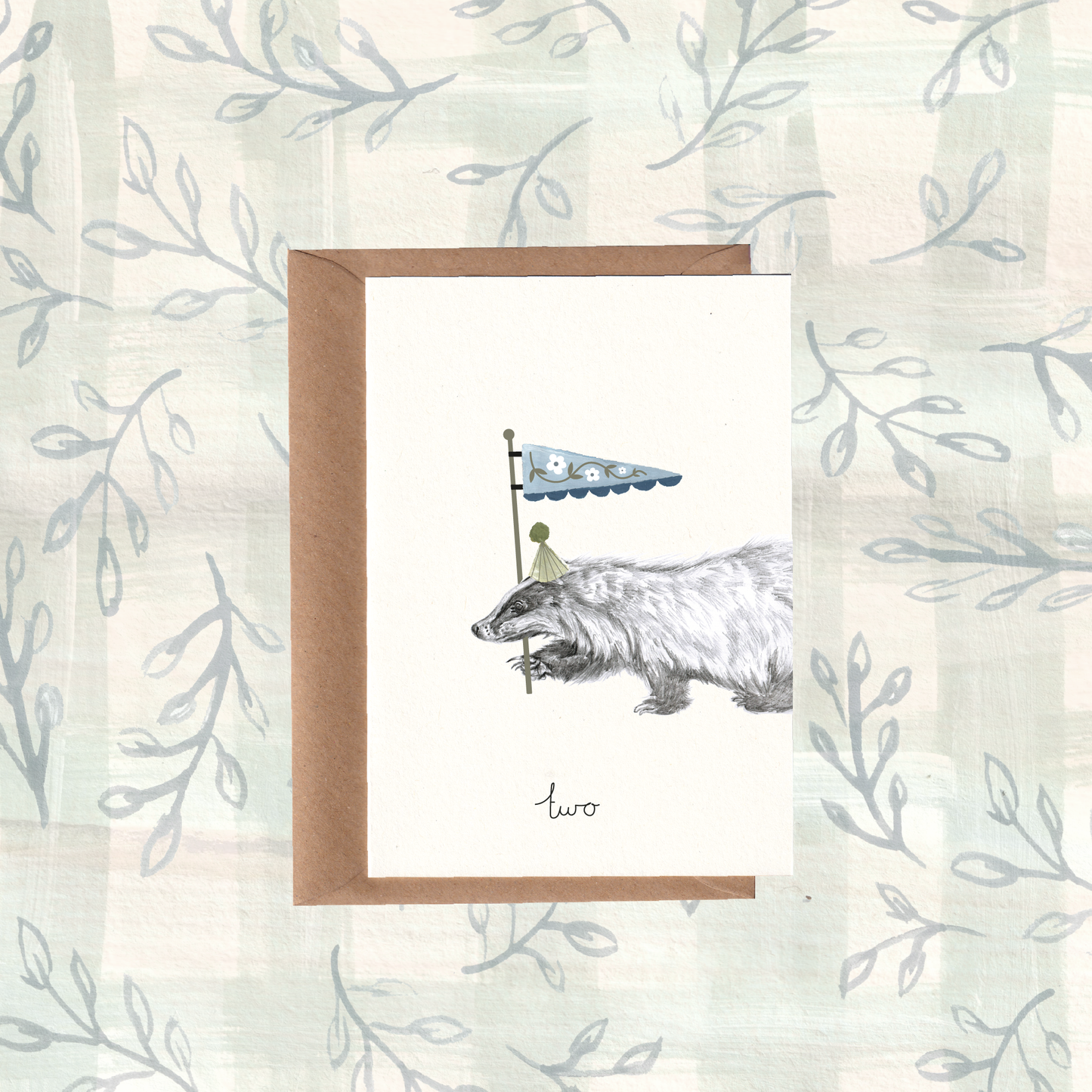 Greeting card with an illustration of a badger waving a flag, set against a woodland background, with a Kraft brown envelope.